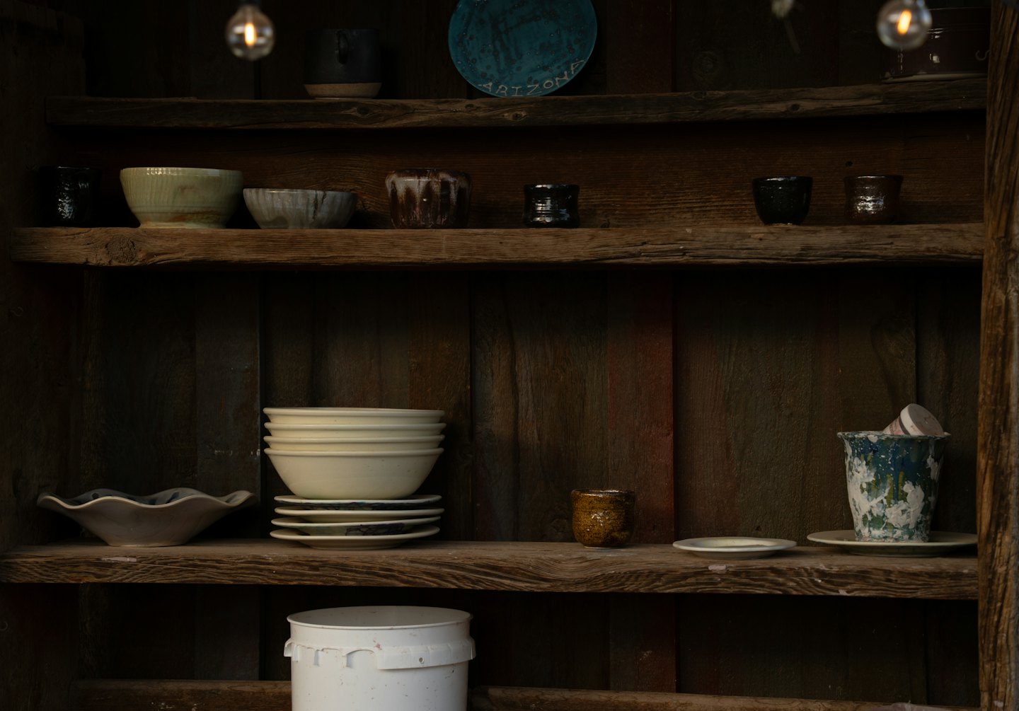 Handcrafted ceramic bowls, plates, and cups on rustic wooden shelves.