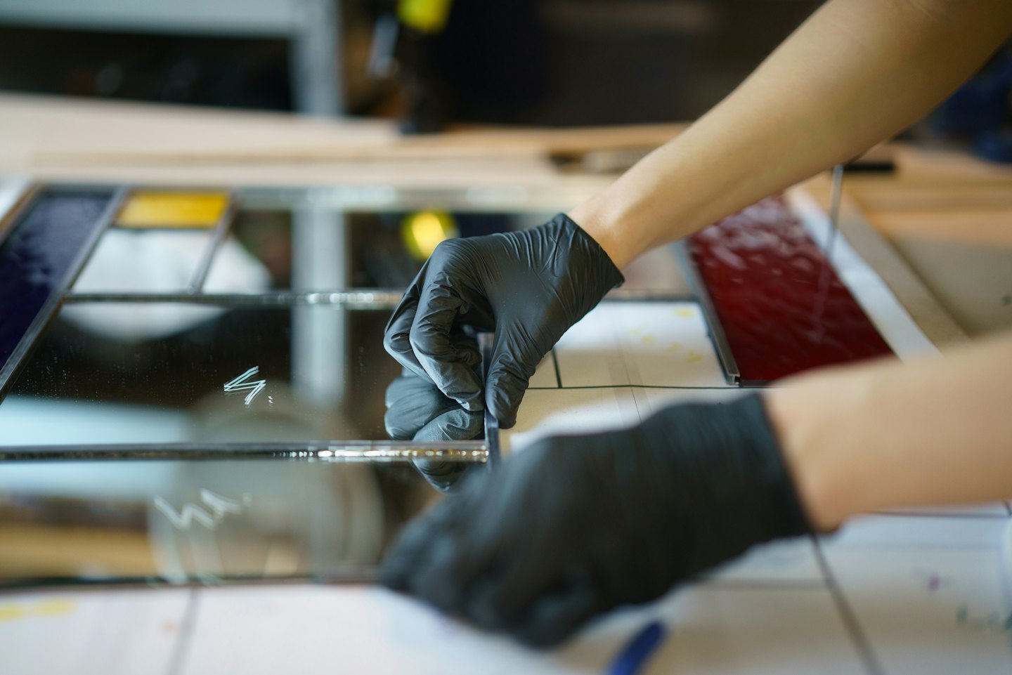 Gloved hands assembling a colorful stained glass panel.